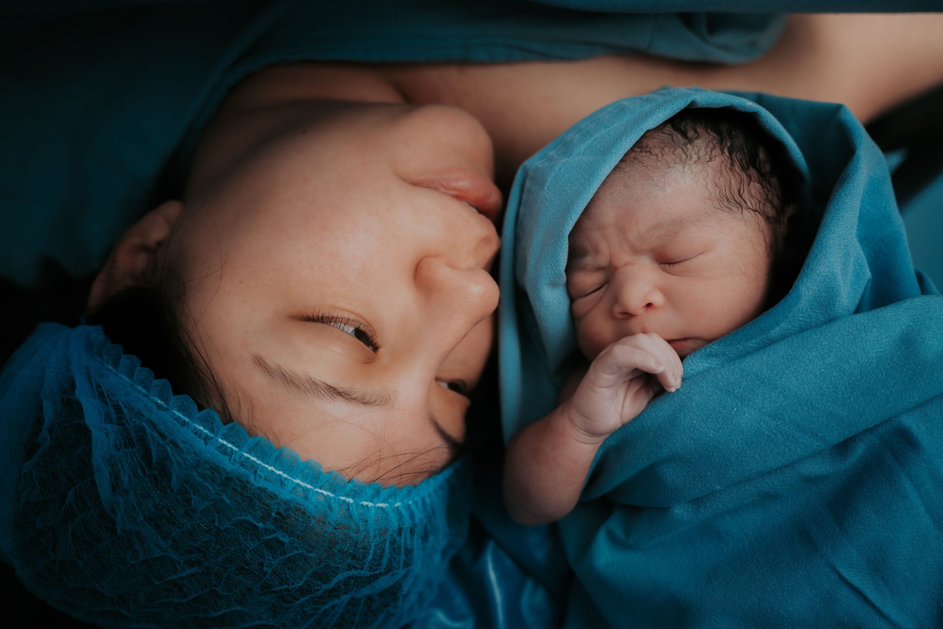 Einrührendes Bild einer Mutter und ihres neugeborenen Babys, eingewickelt in blaue medizinische Decken.