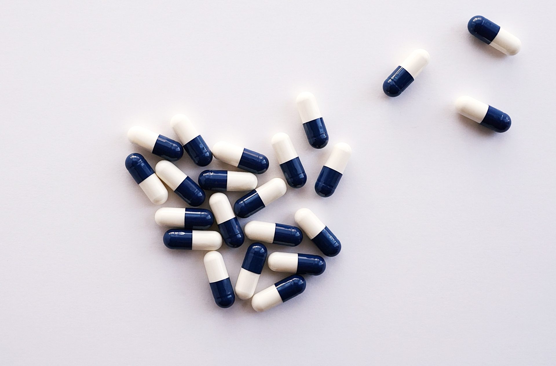 Draufsicht auf blau-weiße Kapseln, die auf einer weißen Fläche angeordnet sind – ideal für Themen aus den Bereichen Gesundheitswesen und Medizin.