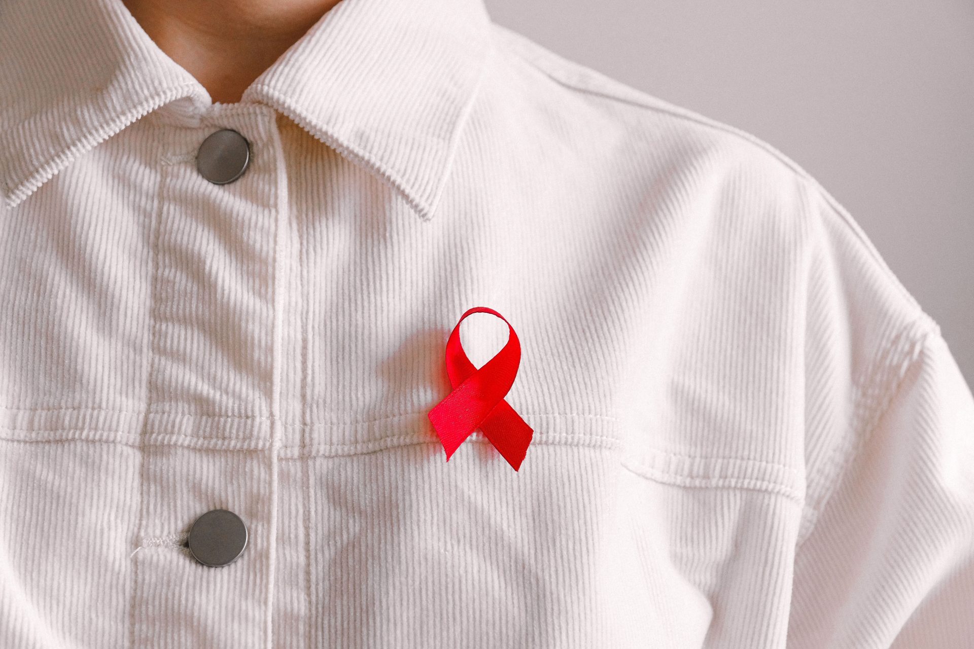 Eine rote Schleife zur Sensibilisierung für HIV/AIDS, an ein weißes Hemd geheftet, als Symbol für Unterstützung und Solidarität.