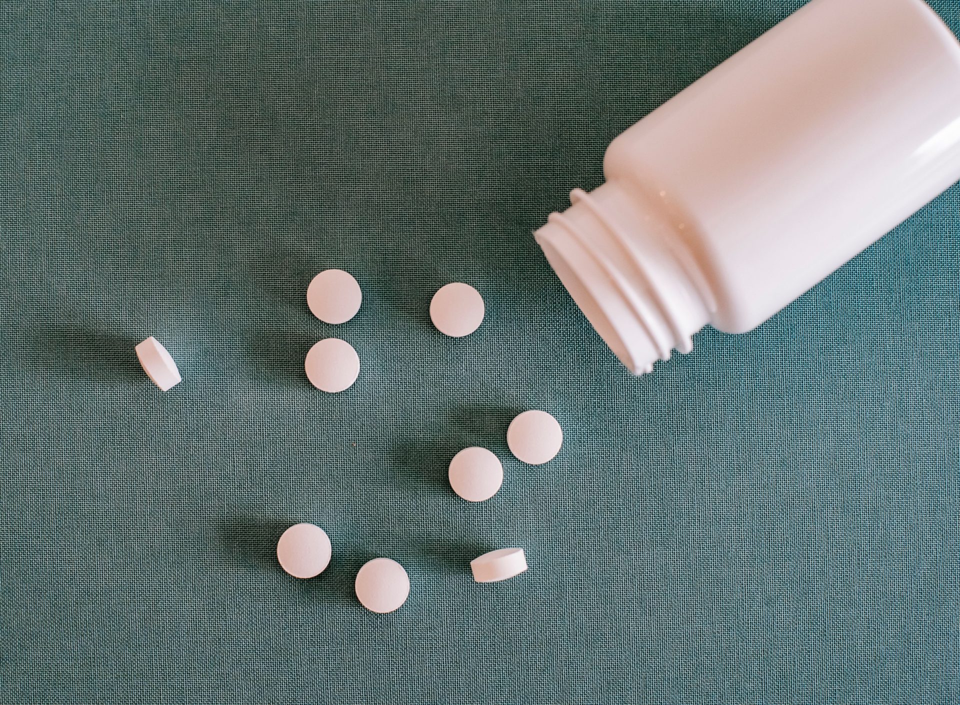Draufsicht auf ähnliche, runde, weiße Tabletten, die aus einem Kunststoffbehälter auf einen Tisch geschüttet wurden.