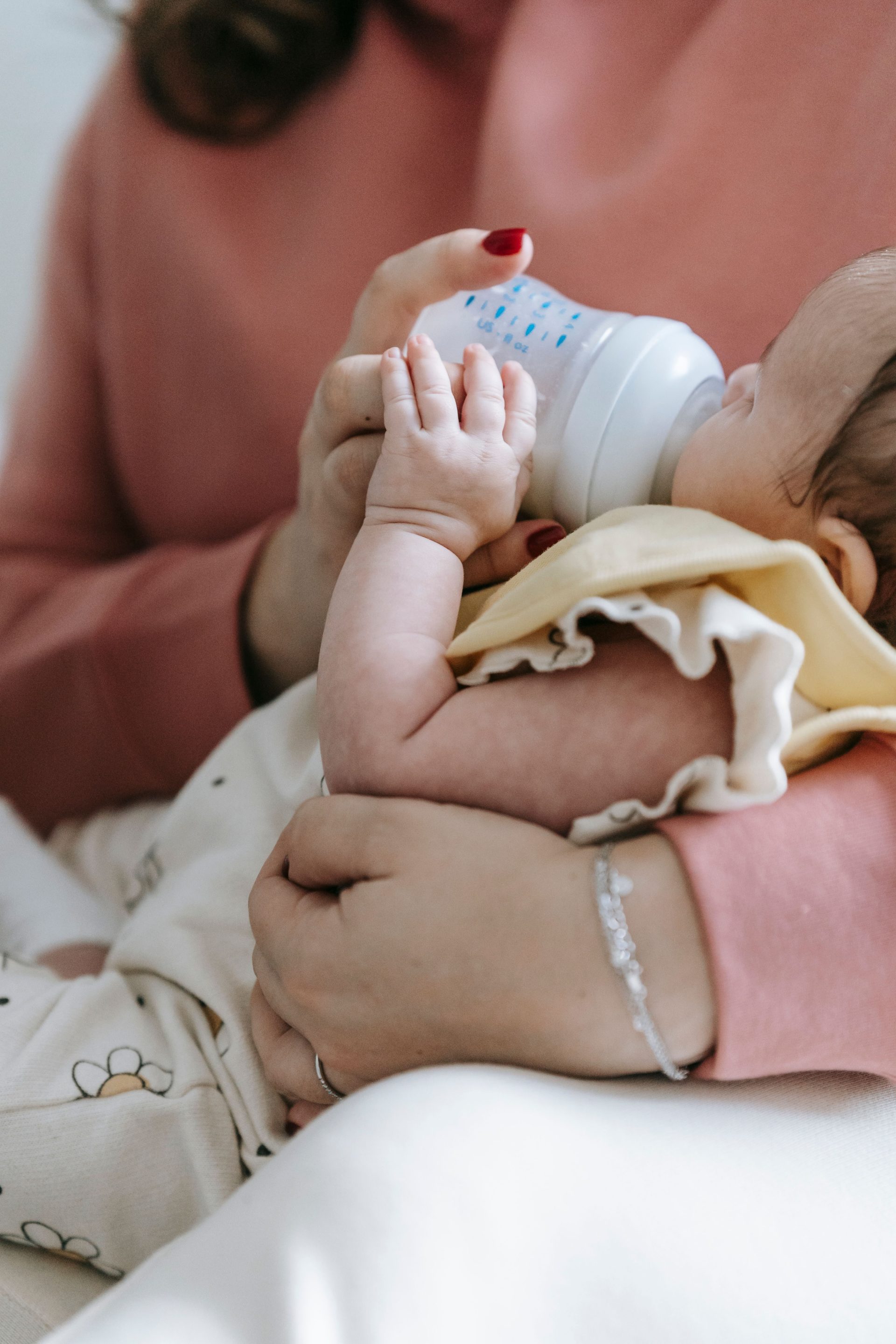 Nahaufnahme einer Mutter in Freizeitkleidung, die ihr niedliches Baby im Arm hält und ihm in einem hellen Zimmer zu Hause die Flasche gibt (Ausschnitt).