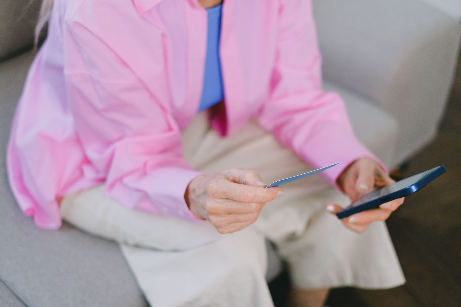 Eine ältere Frau hält eine Kreditkarte und ein Smartphone für den Online-Einkauf in der Hand.