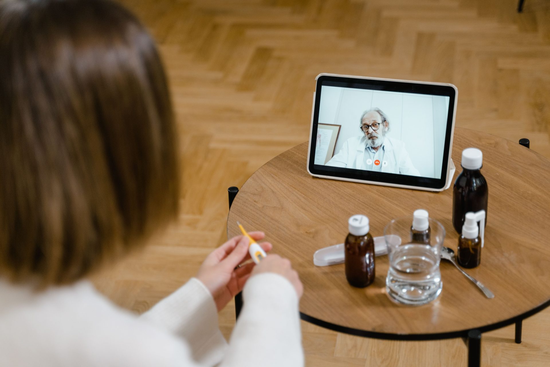 Ein Arzt führt eine Online-Beratung per Videoanruf auf einem Tablet durch, das auf einem Holztisch liegt.