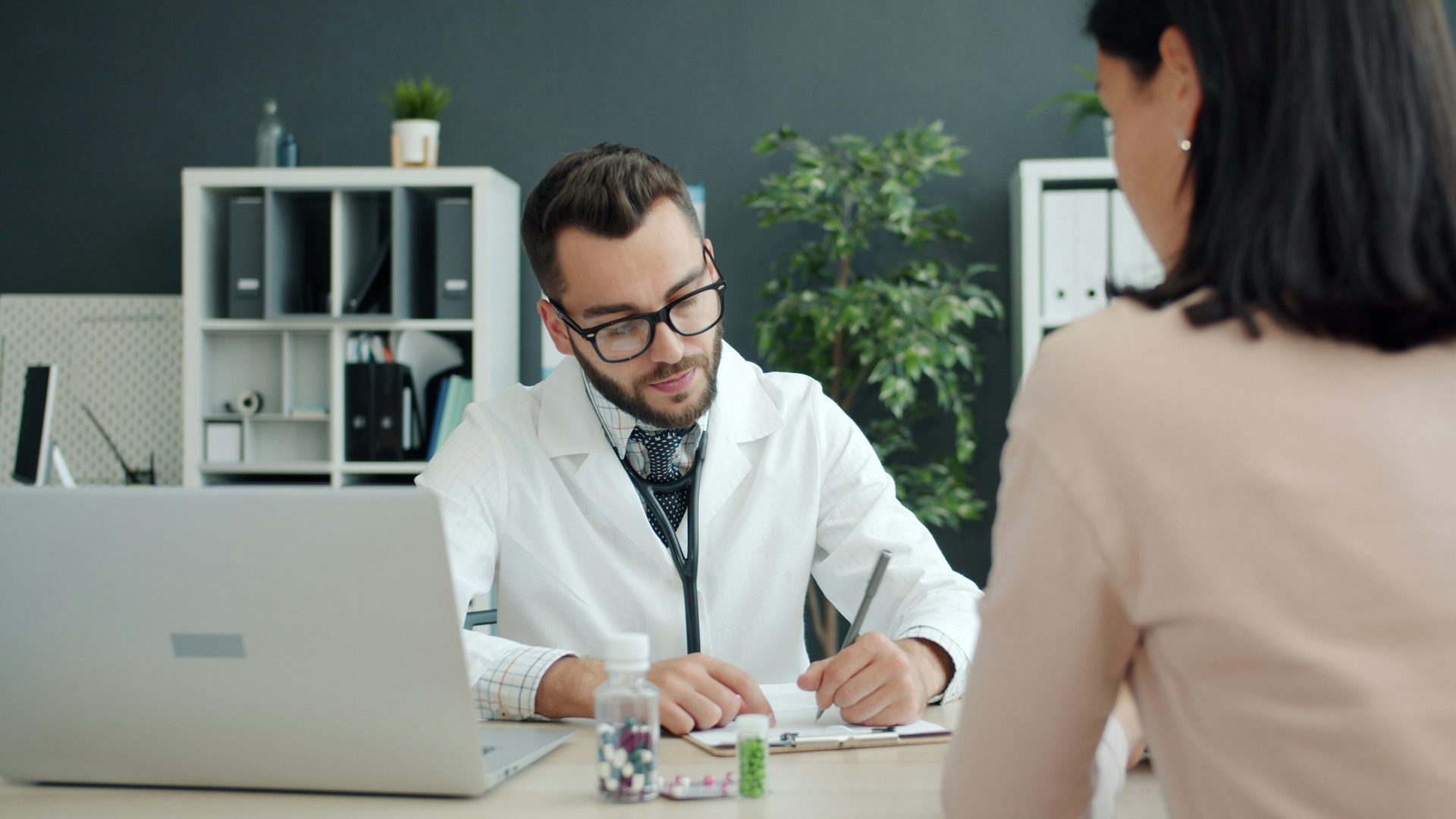 Arzt macht sich Notizen, während der Patient ihm gegenüber sitzt.