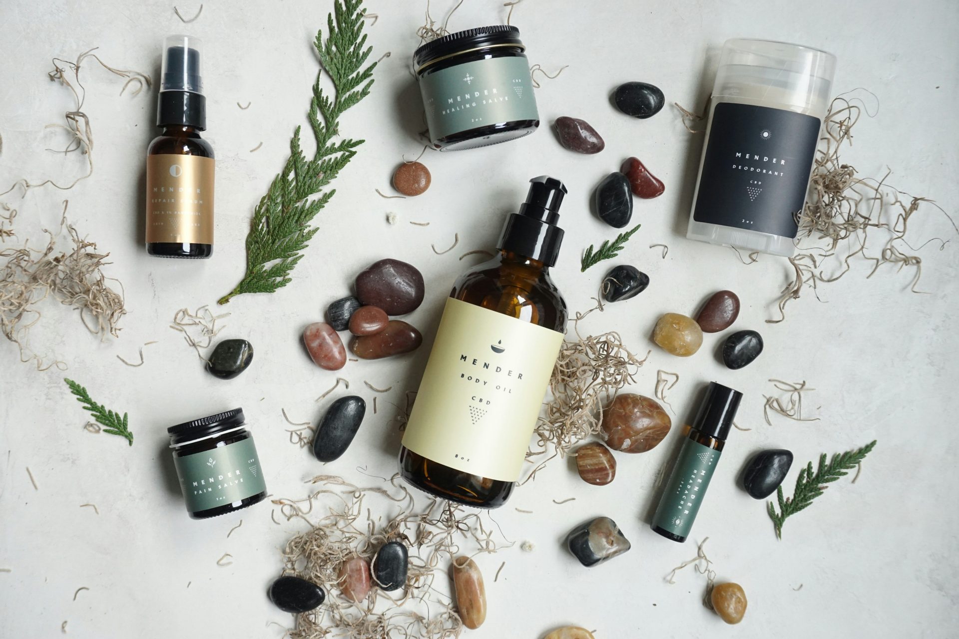 Skincare products with smooth river stones and evergreen sprigs on a light surface